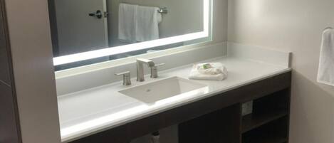 A bathroom with a large mirror, a sink, and a towel rack.