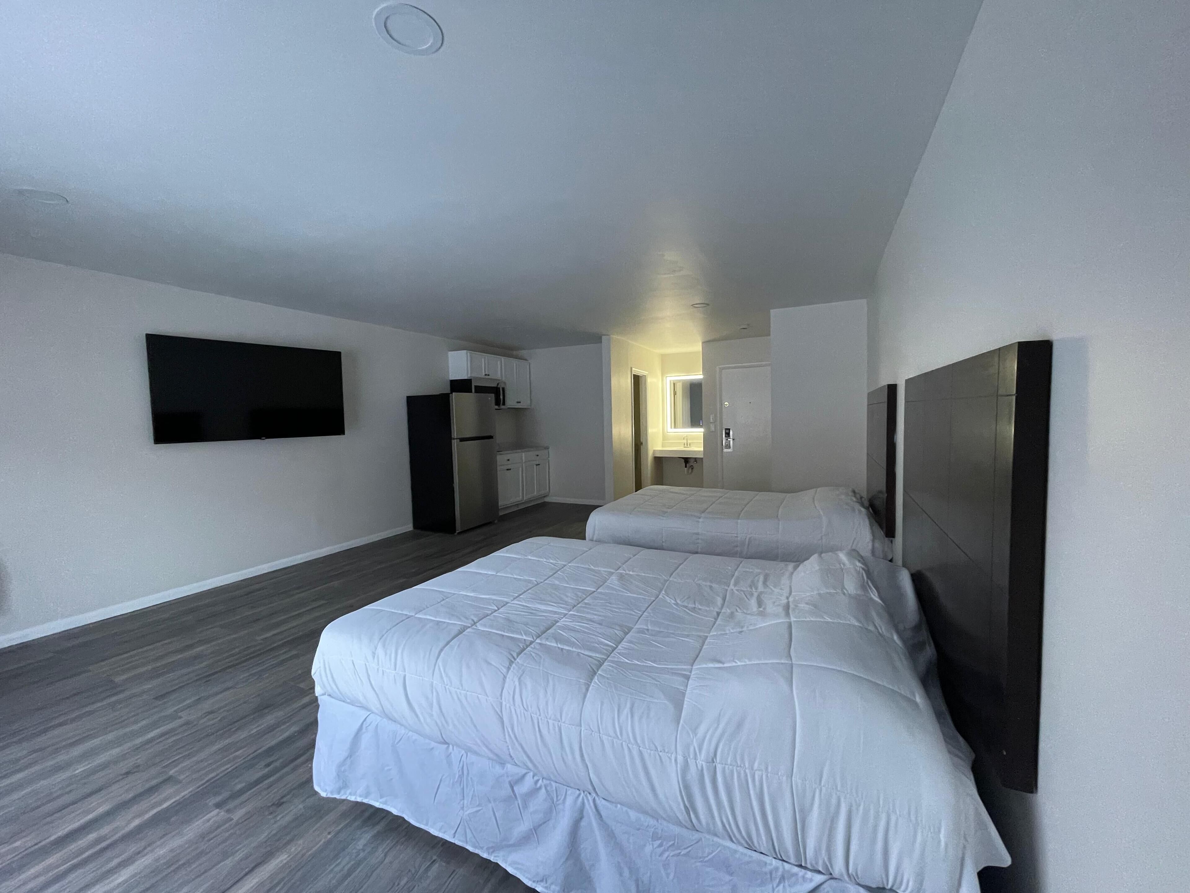Une chambre d’hôtel moderne dotée d’un grand lit, d’un téléviseur à écran plat fixé au mur, d’un réfrigérateur et d’un four à micro-ondes.