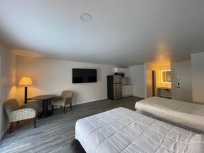 A hotel room with two beds, a small table with a chair, a TV mounted on the wall, a refrigerator, and a microwave. - St. Croix Suites - St. Croix Falls (St Croix Falls)