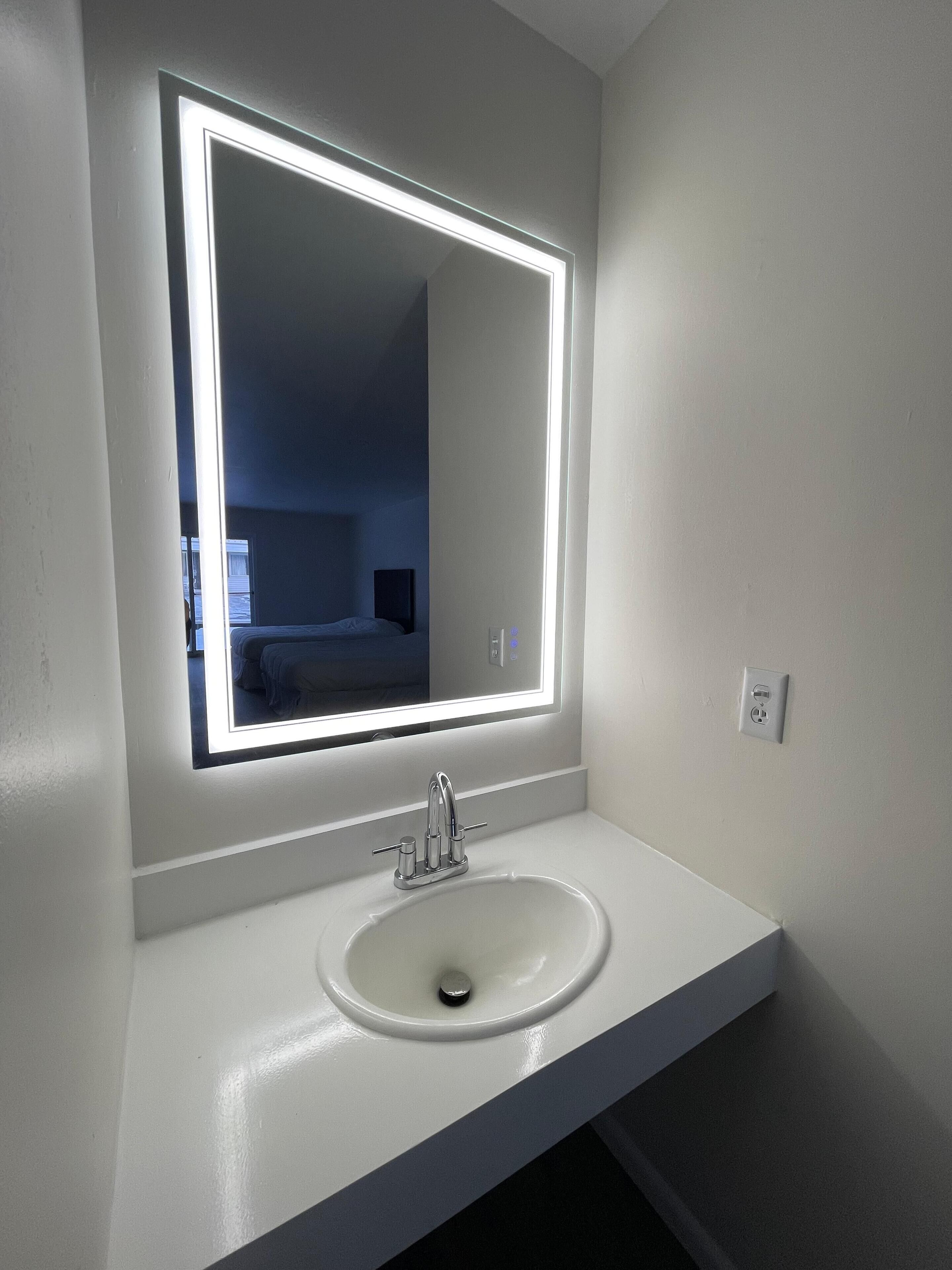 A bathroom with a white sink, a mirror with a lighted frame, and a visible power outlet.