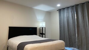 A hotel room with a bed, a nightstand, a lamp, and a window with curtains. - St. Croix Suites - St. Croix Falls (St Croix Falls)