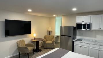 Habitación de hotel con cama, televisor, refrigerador, microondas, una mesita con lámpara y dos sillas.