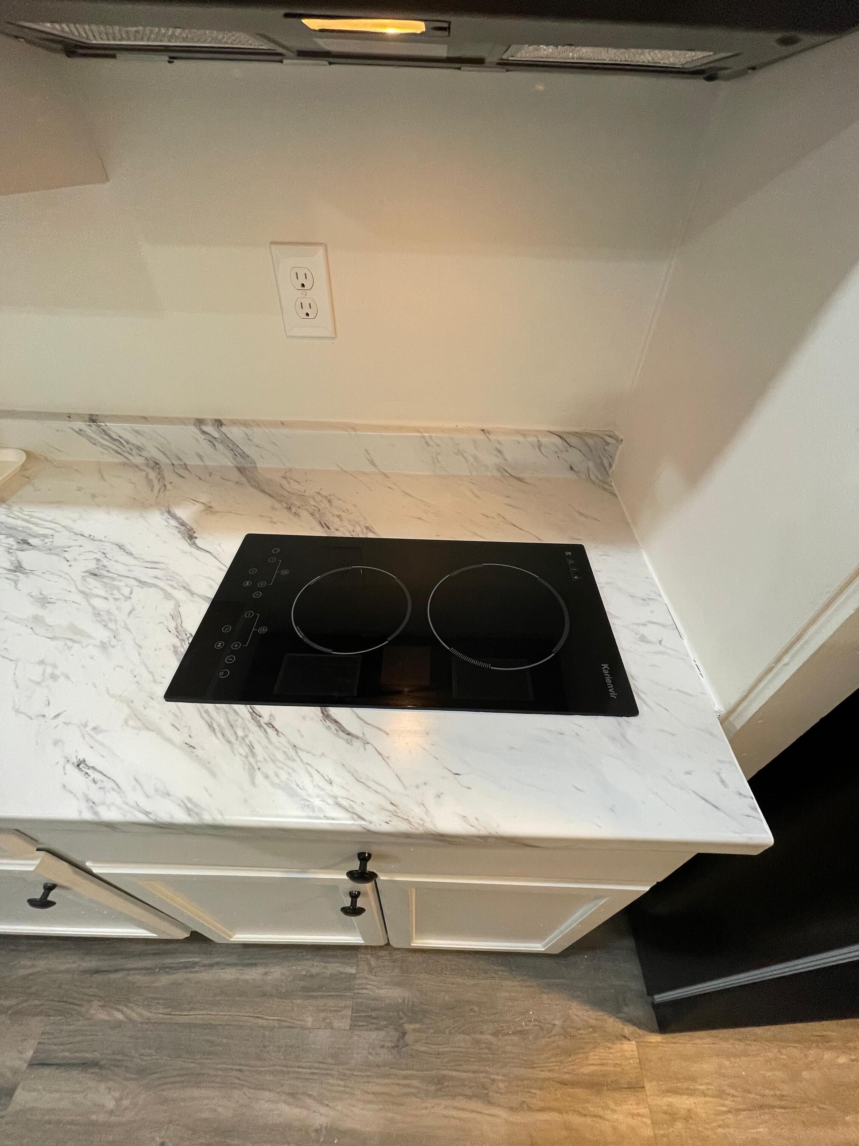 A kitchen with a white marble countertop, two black induction cooktops, and a white cabinet below.