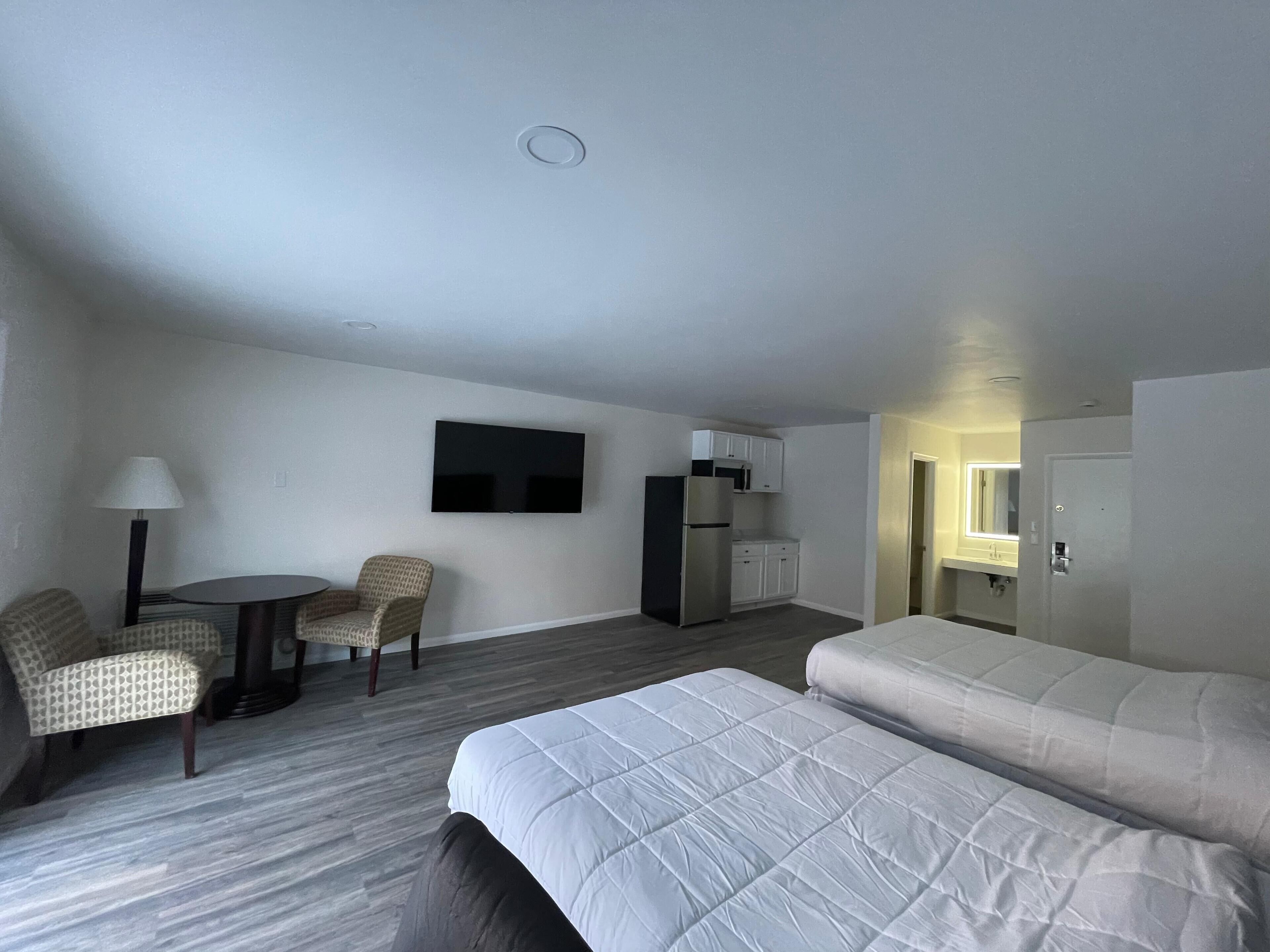 A hotel room with a bed, two chairs, a small table, a TV, a refrigerator, and a kitchenette.