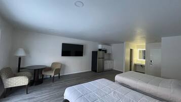 A hotel room with a bed, two chairs, a small table, a TV, a refrigerator, and a kitchenette.