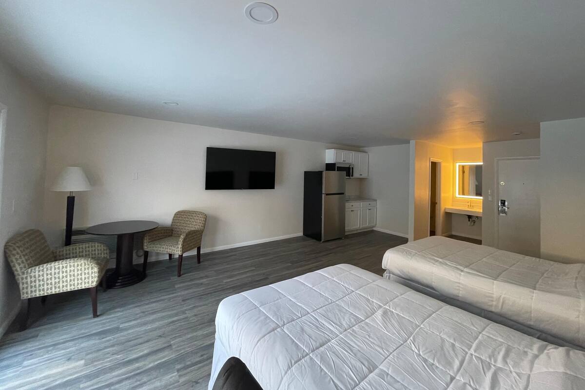 A hotel room with a bed, a desk with chairs, a television, a refrigerator, and a small kitchenette.