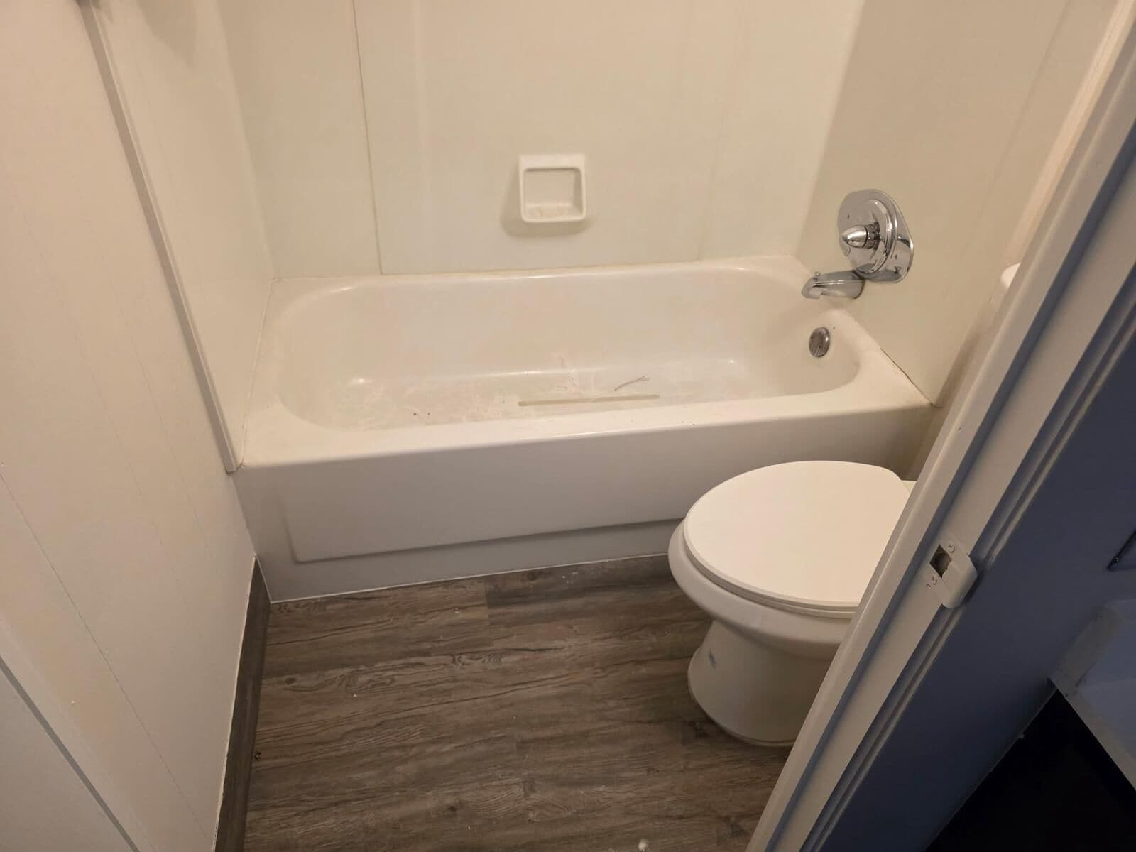 A small bathroom with a white bathtub, a toilet, and a wooden floor.