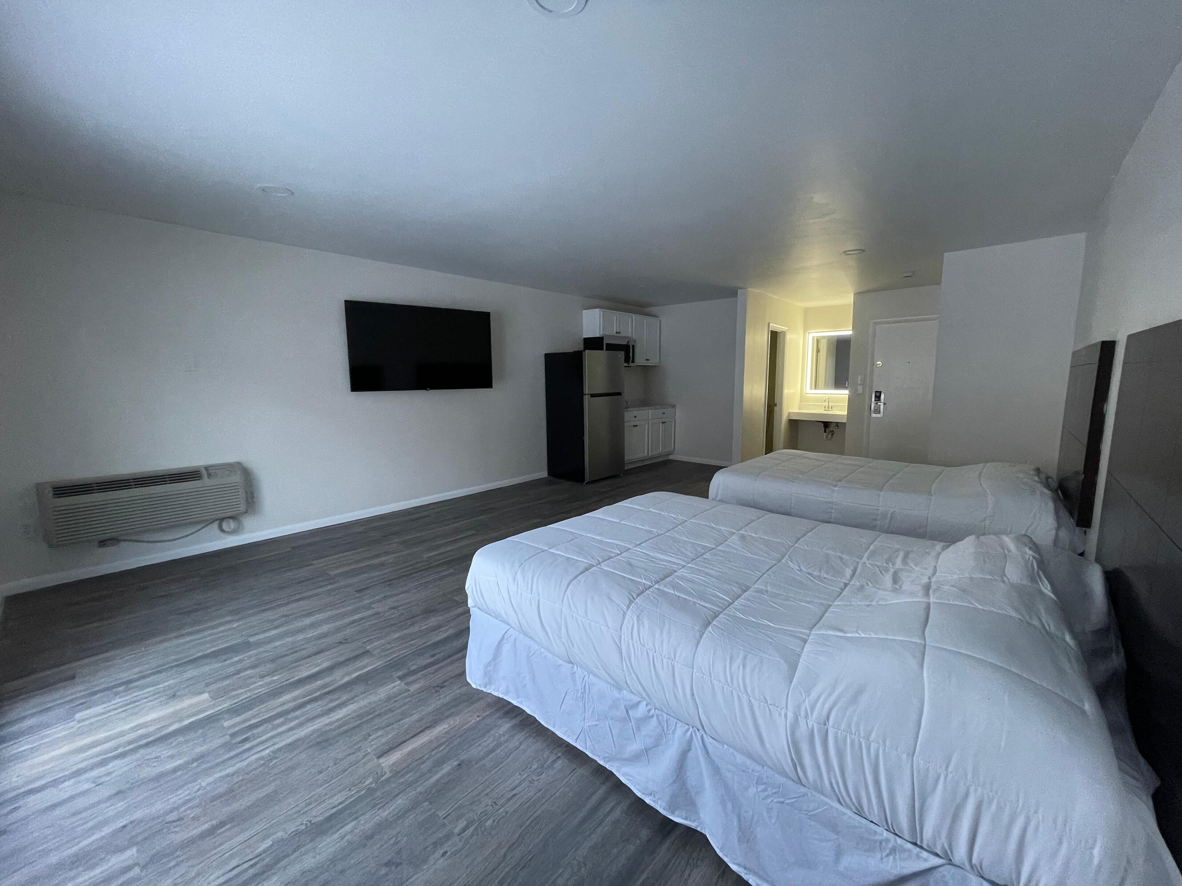 Quarto de hotel com duas camas, televisão de tela plana, mini-geladeira, micro-ondas e uma pequena cozinha.
