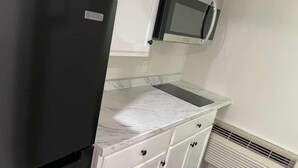 A kitchen with a black refrigerator, white cabinets, a microwave, and a marble countertop. - St. Croix Suites - St. Croix Falls (St Croix Falls)
