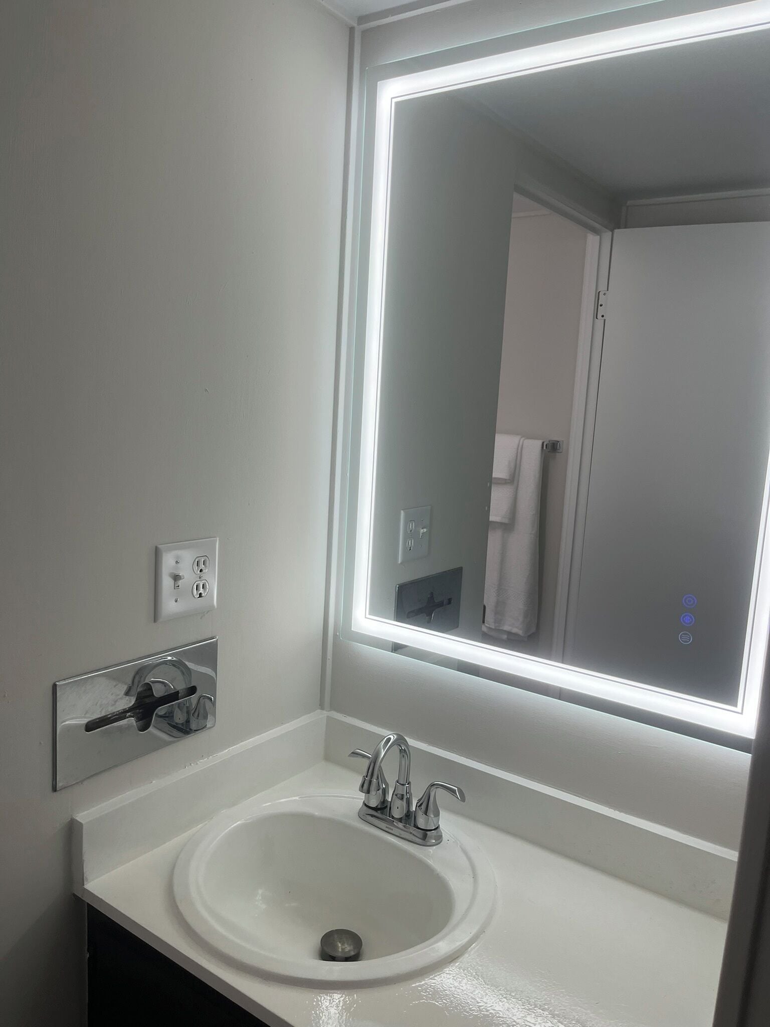 Un bagno con un lavandino bianco, uno specchio con illuminazione a LED e un portasciugaussignia.
