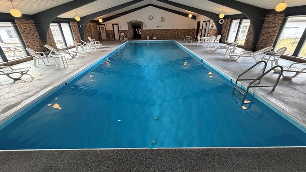An indoor swimming pool with clear water, surrounded by lounge chairs and a high ceiling with exposed beams. - St. Croix Suites - St. Croix Falls (St Croix Falls)
