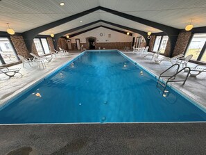 An indoor swimming pool with clear water, surrounded by lounge chairs and a high ceiling with exposed beams. - St. Croix Suites - St. Croix Falls (St Croix Falls)