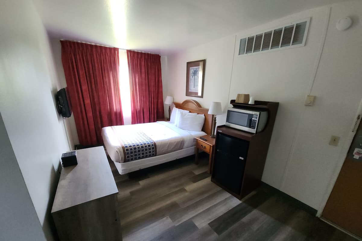 A hotel room with a bed, a desk, a microwave, and a small refrigerator.