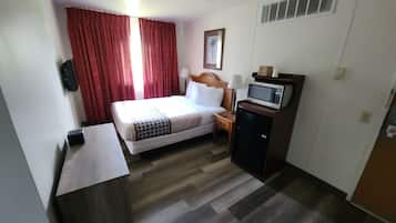 A hotel room with a bed, a desk, a microwave, and a small refrigerator.