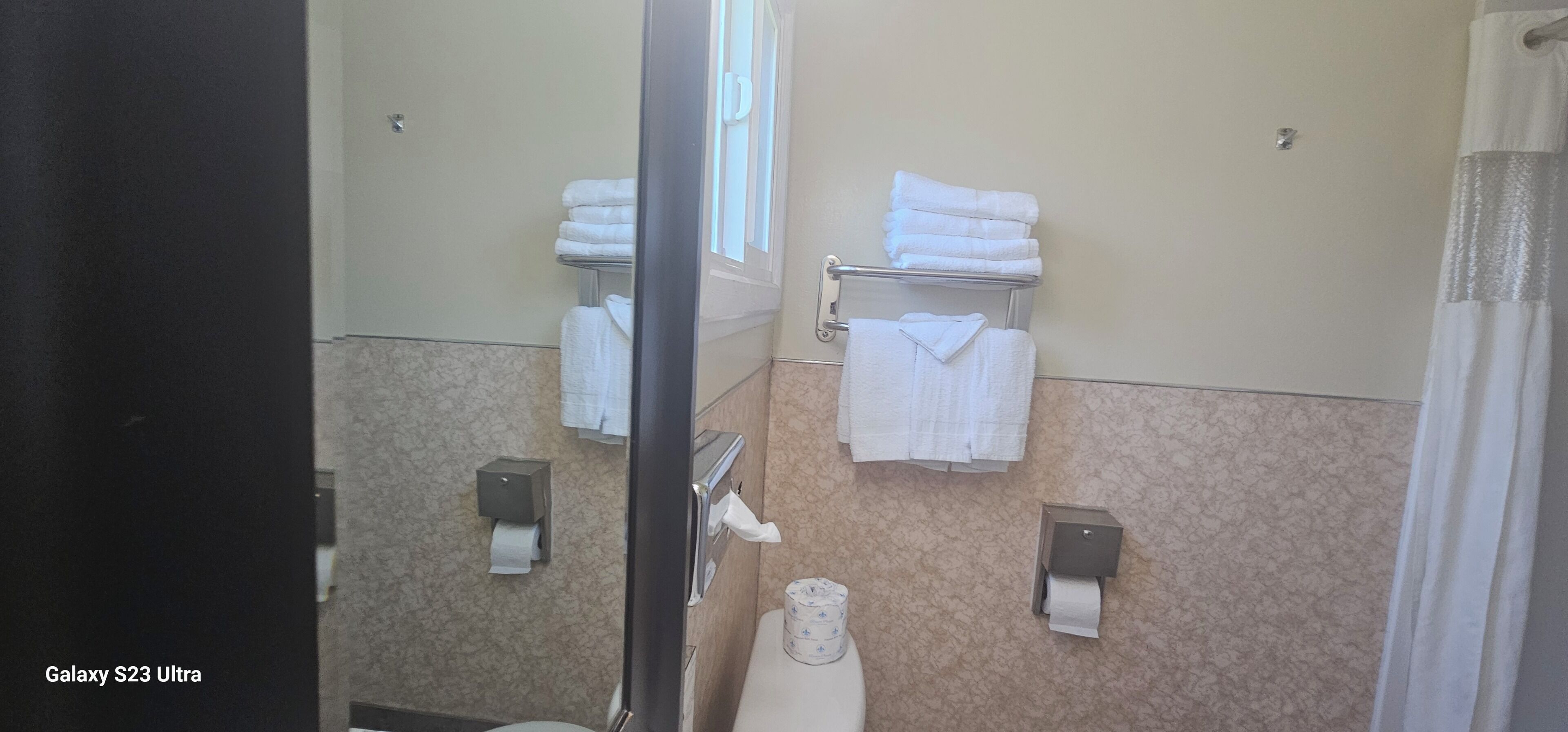 A bathroom with a toilet, two towel racks with folded towels, and two paper towel dispensers.
