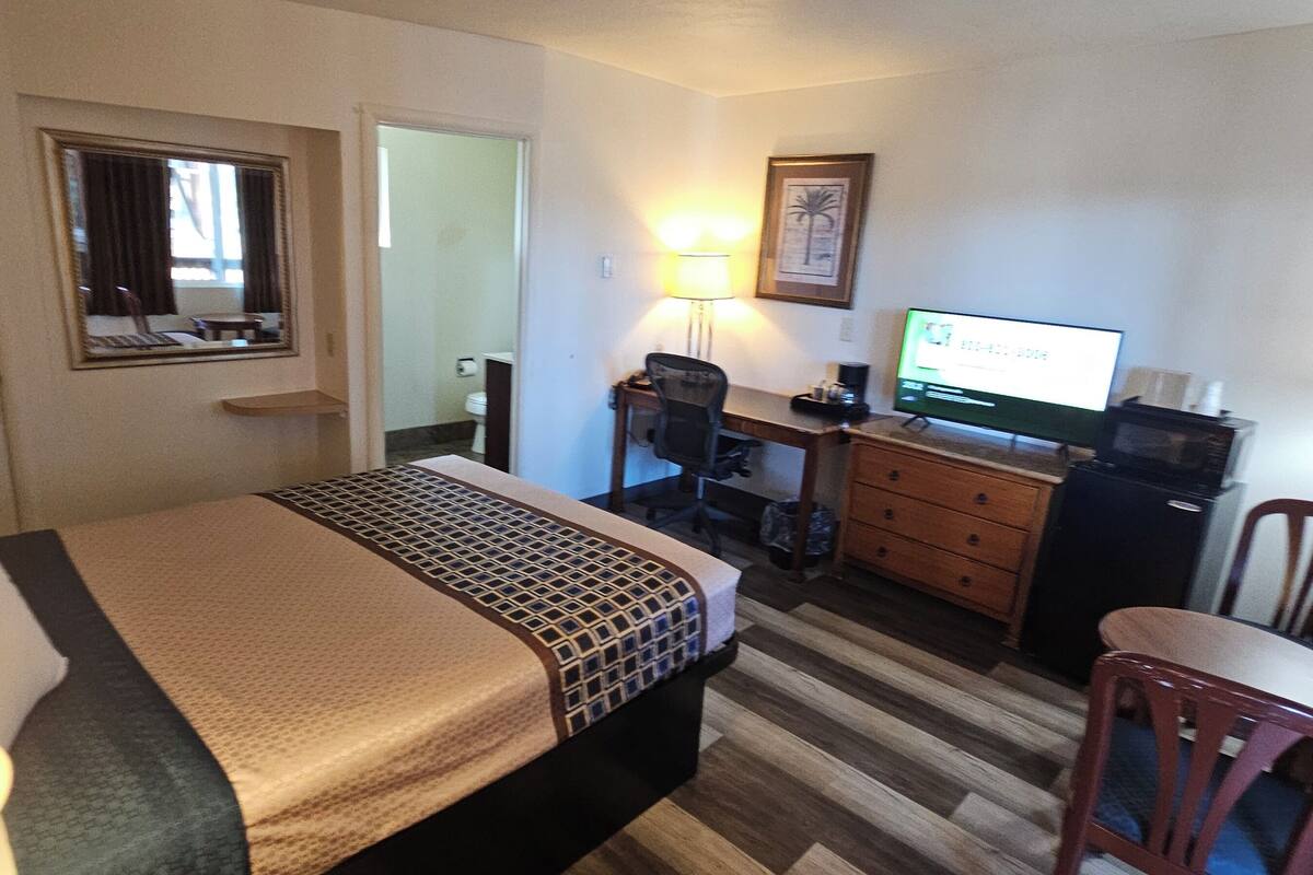 A hotel room with a bed, desk, chair, television, and a small table.