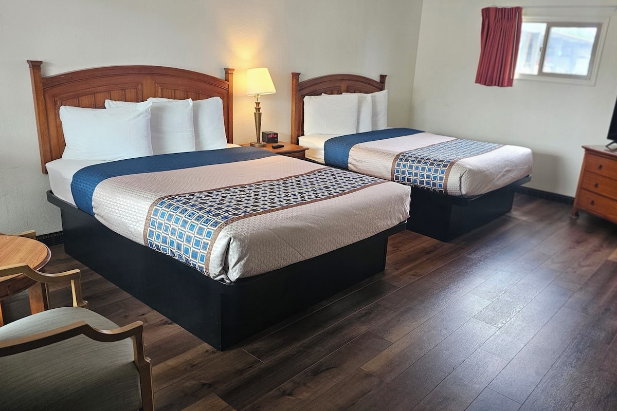 A hotel room with two beds, a desk, a chair, a TV, and a window with curtains.