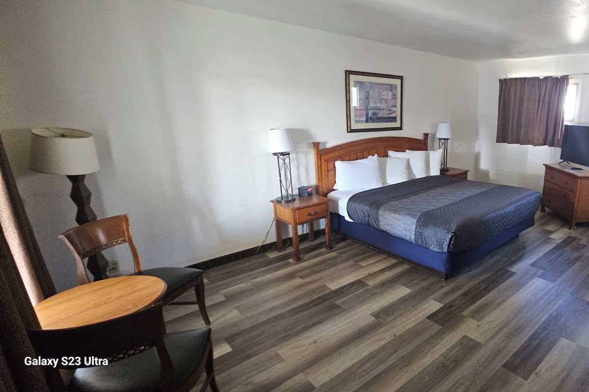 A hotel room with a bed, a desk, a chair, a lamp, a television, and a framed picture on the wall.