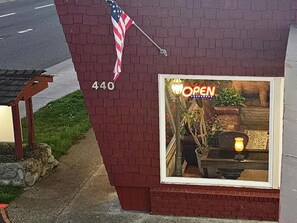 A brick building with an American flag, a storefront with an 'OPEN' sign, and a window displaying a plant and a lamp. - North Coast Inn (Crescent City)