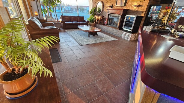 Uma sala de estar ampla com um sofá de couro, uma mesa de centro e uma lareira. Há plantas em vasos e uma grande janela com vista para o exterior.