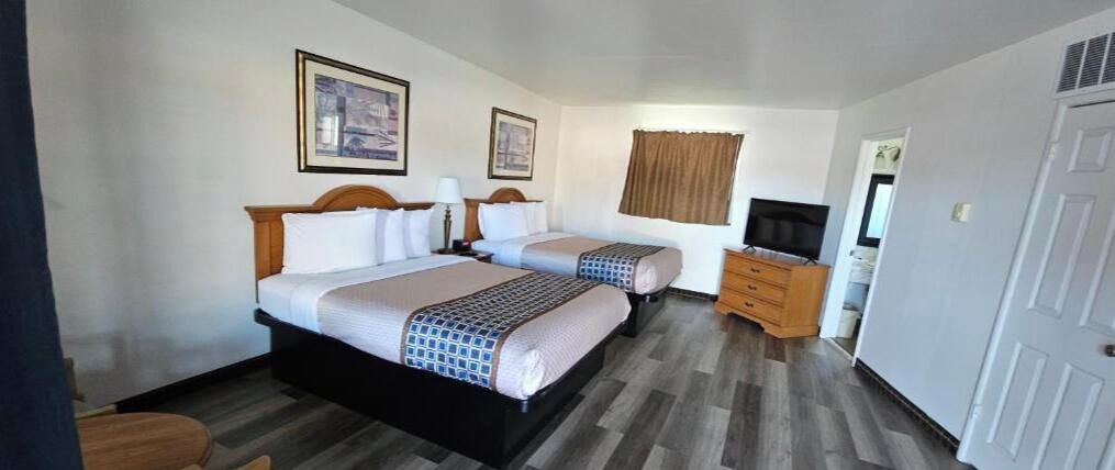 A hotel room with two beds, a television, a dresser, and a door.