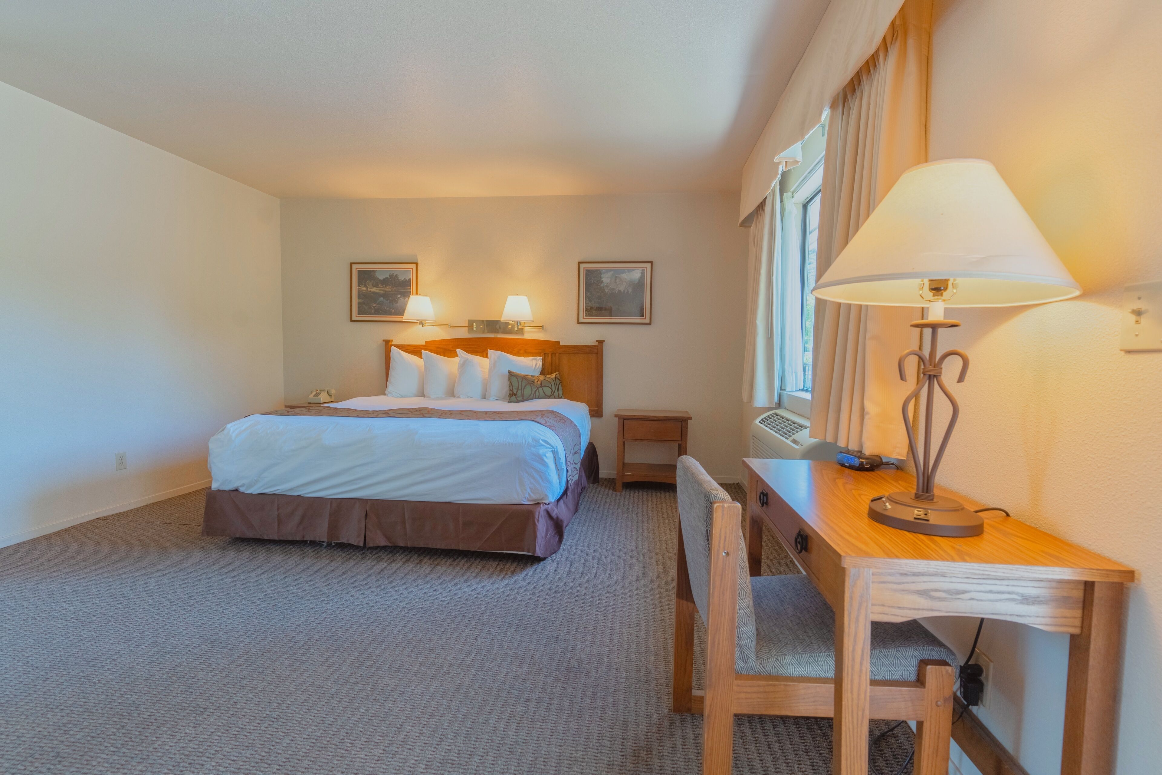 A hotel room with a bed, bedside tables, a desk with a lamp, and a chair.