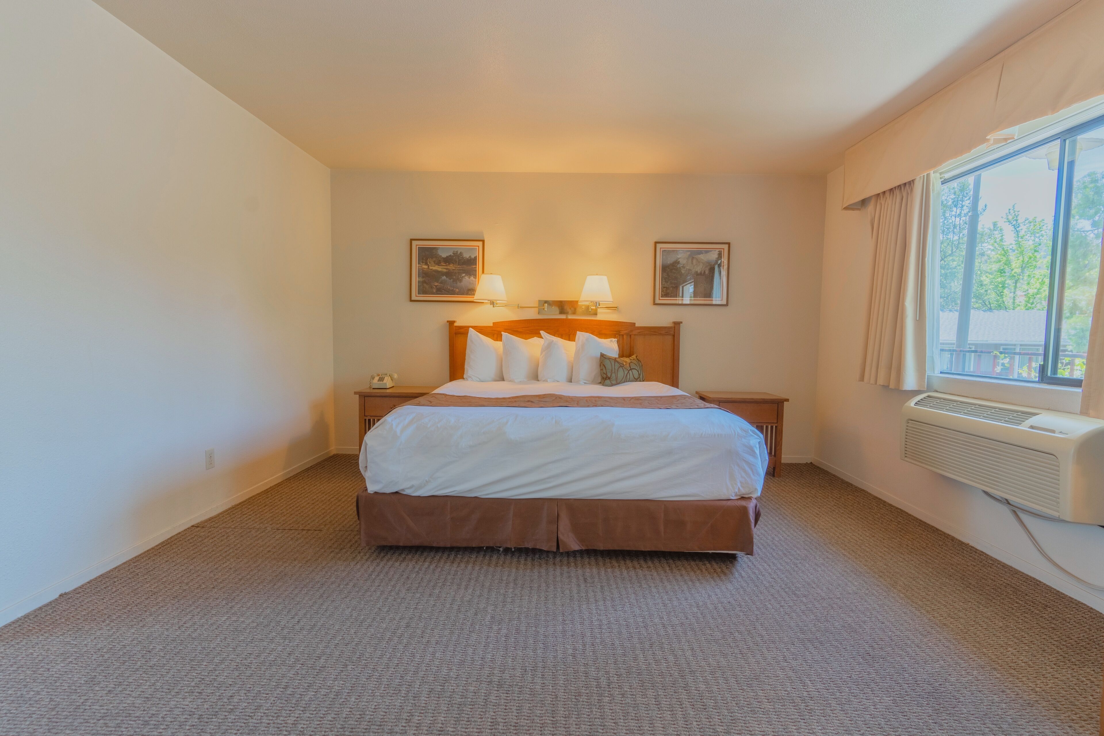 Una habitación de hotel con una cama grande, dos lámparas de noche, una ventana con cortinas y aire acondicionado instalado en la pared.