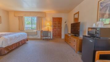 A hotel room with a bed, a desk, a chair, a dresser, a television, a refrigerator, and a window with curtains.