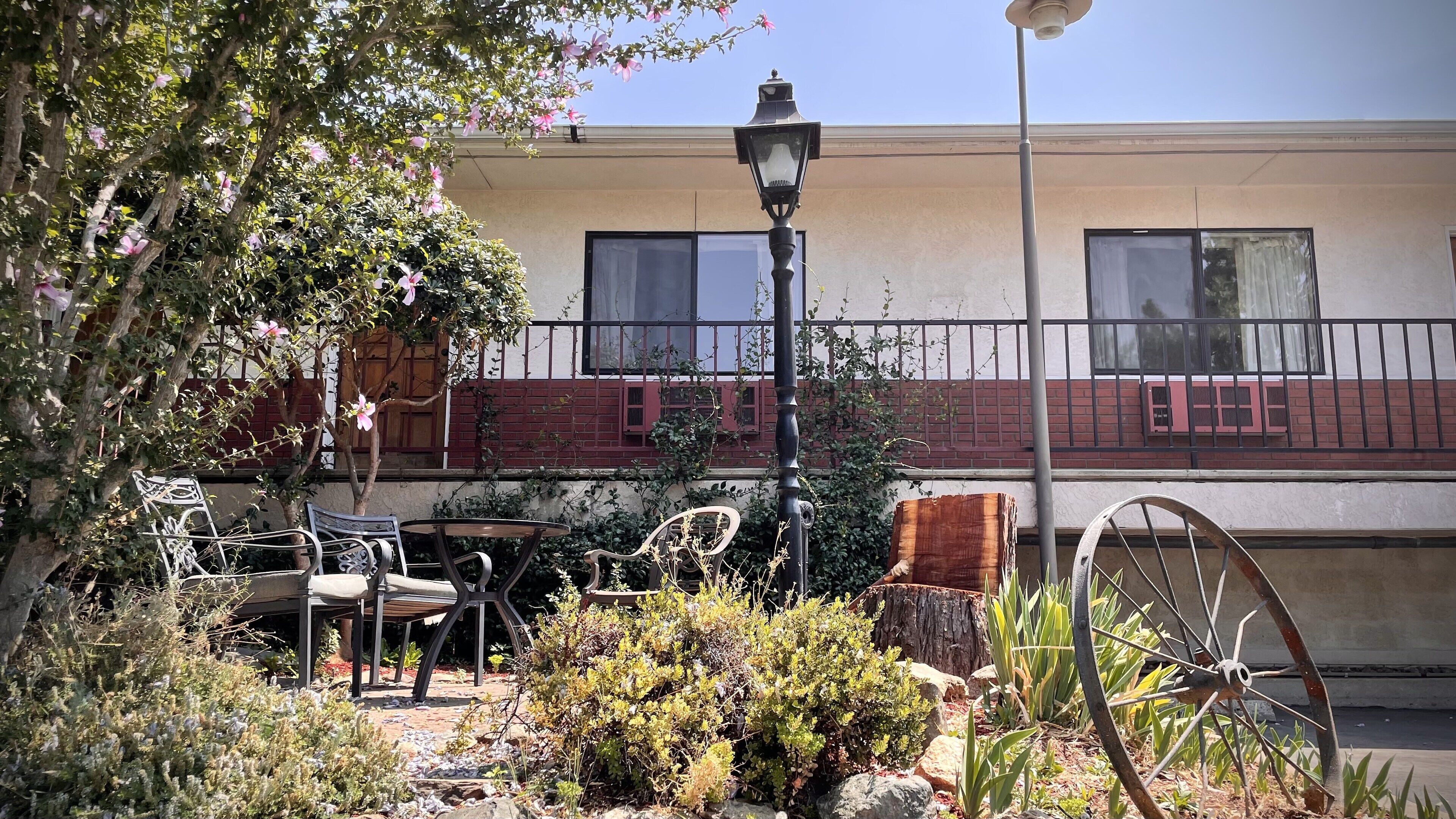 A courtyard with a metal table and chairs, a vintage wagon wheel, and a street lamp.