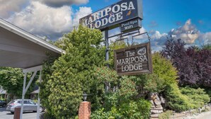 A Mariposa Lodge sign with amenities listed, surrounded by lush greenery and a clear sky. - Mariposa Lodge (Mariposa)