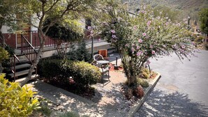 A patio area with a table and chairs, surrounded by lush greenery and flowering plants. - Mariposa Lodge (Mariposa)