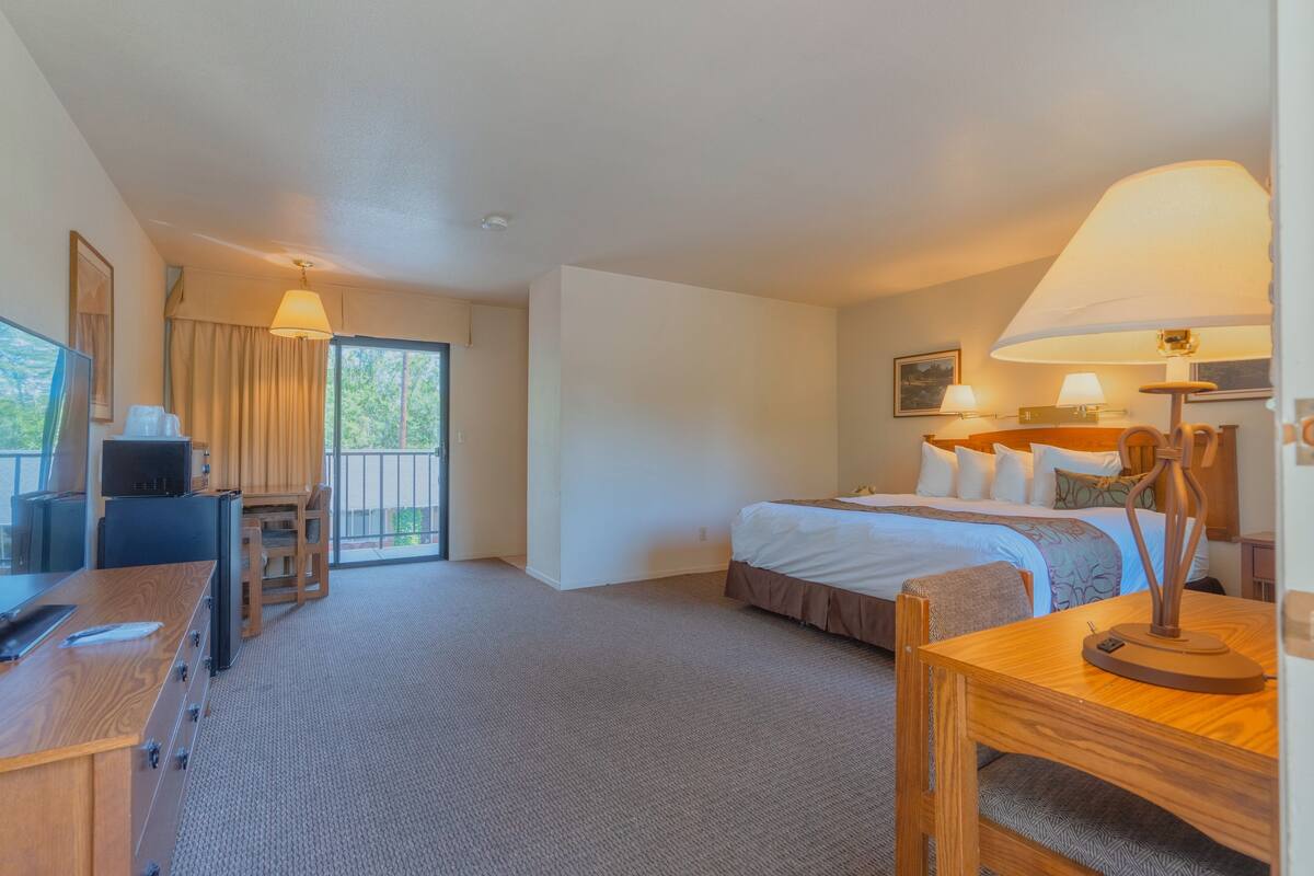 A hotel room with a bed, a desk with a computer, a lamp, and a view of the outdoors.
