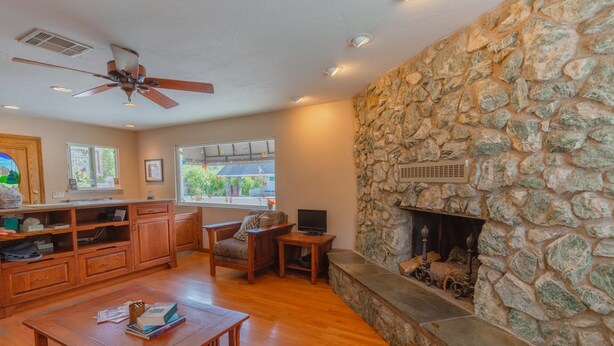 A spacious living room with a stone fireplace, wooden furniture, and a ceiling fan. - Mariposa Lodge (Mariposa)