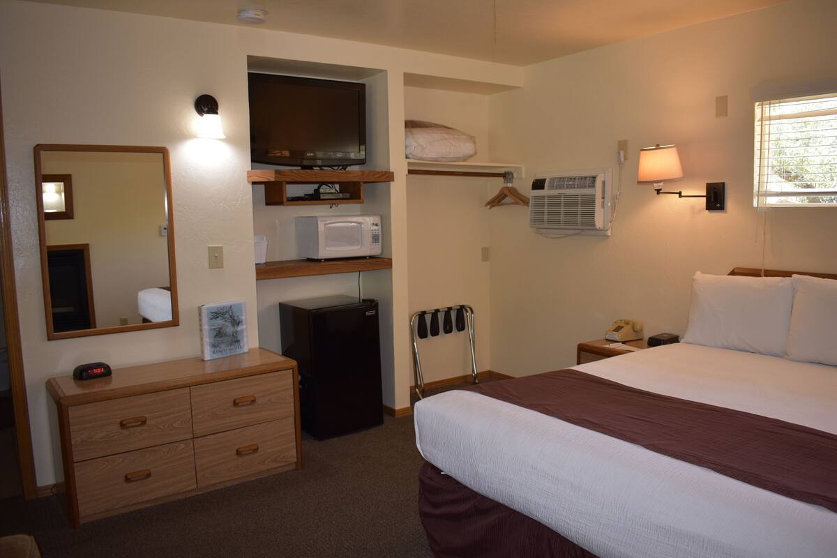 Une chambre d’hôtel équipée d’un lit, d’une commode, d’un four à micro-ondes, d’un réfrigérateur, d’une télévision et d’une fenêtre avec des stores.