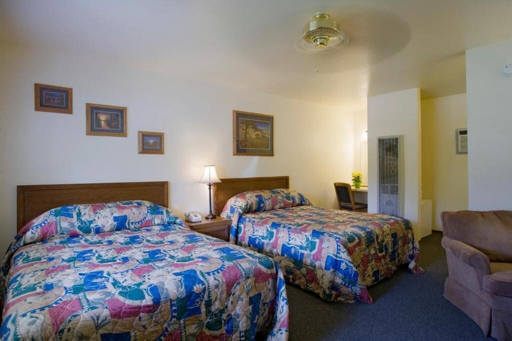 Ein Hotelzimmer mit zwei Betten, einem Schreibtisch, einem Stuhl und einem Deckenventilator.