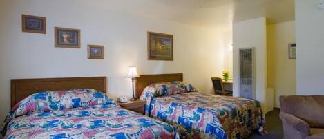 Ein Hotelzimmer mit zwei Betten, einem Schreibtisch, einem Stuhl und einem Deckenventilator.