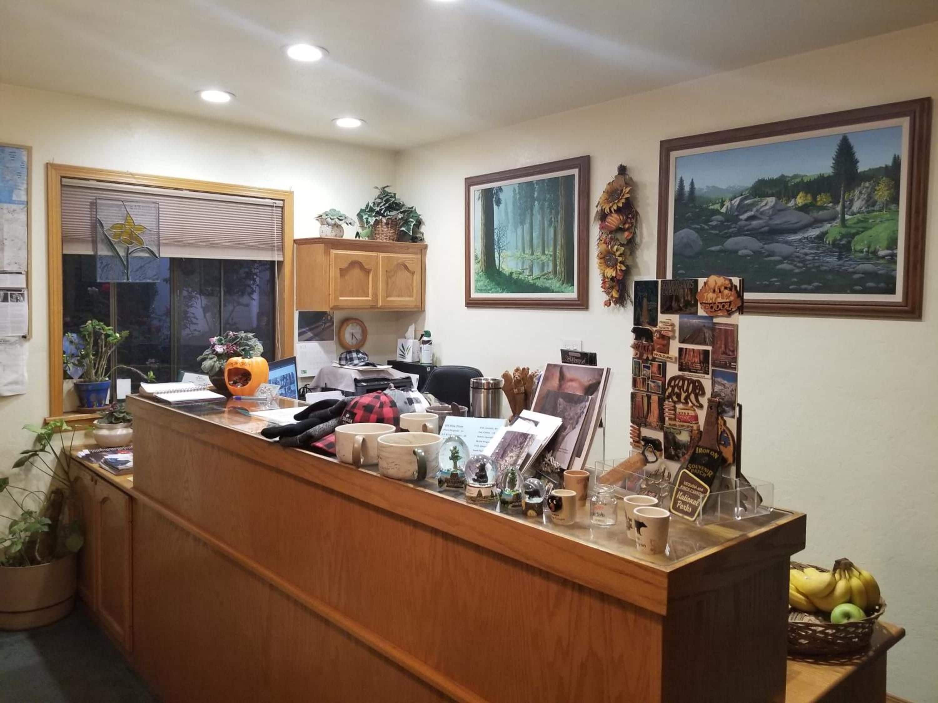 Un mostrador de recepción con una computadora, un reloj y diversos objetos, incluyendo tazas y una cesta de plátanos.