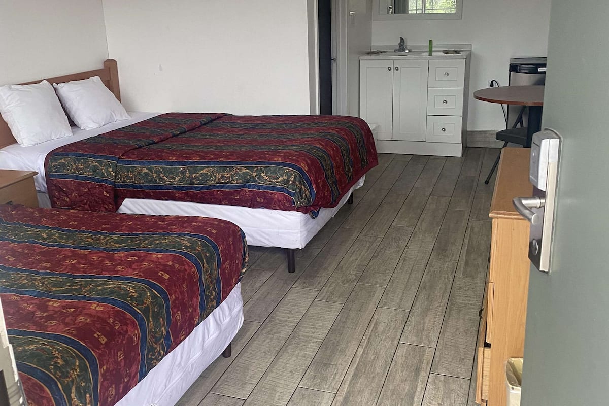 A room with two beds, a small kitchenette, and a bathroom.