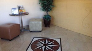 A reception area with a reception desk, a potted plant, a small table with brochures, and a brown ottoman. - Americas Best Value Inn Thousand Oaks (Thousand Oaks)