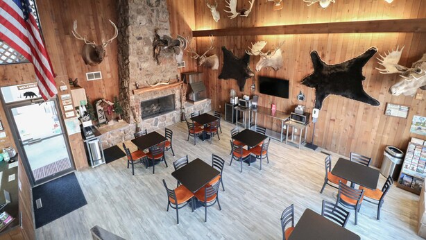Un restaurant aux murs en bois, orné de têtes d’animaux empaillées et doté d’une cheminée en pierre. Les tables et les chaises sont disposées pour accueillir les clients.