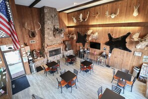 A restaurant with wooden walls, mounted animal heads, and a stone fireplace. Tables and chairs are arranged for dining. - Bear Lodge Motel (Sundance)