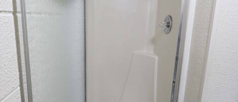 A small, enclosed shower stall with a glass door, a showerhead, and a white towel hanging on the door.