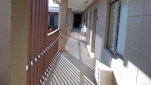 Un couloir bordé d’une clôture en bois d’un côté et d’un mur carrelé de l’autre, qui mène à l’entrée d’un bâtiment.