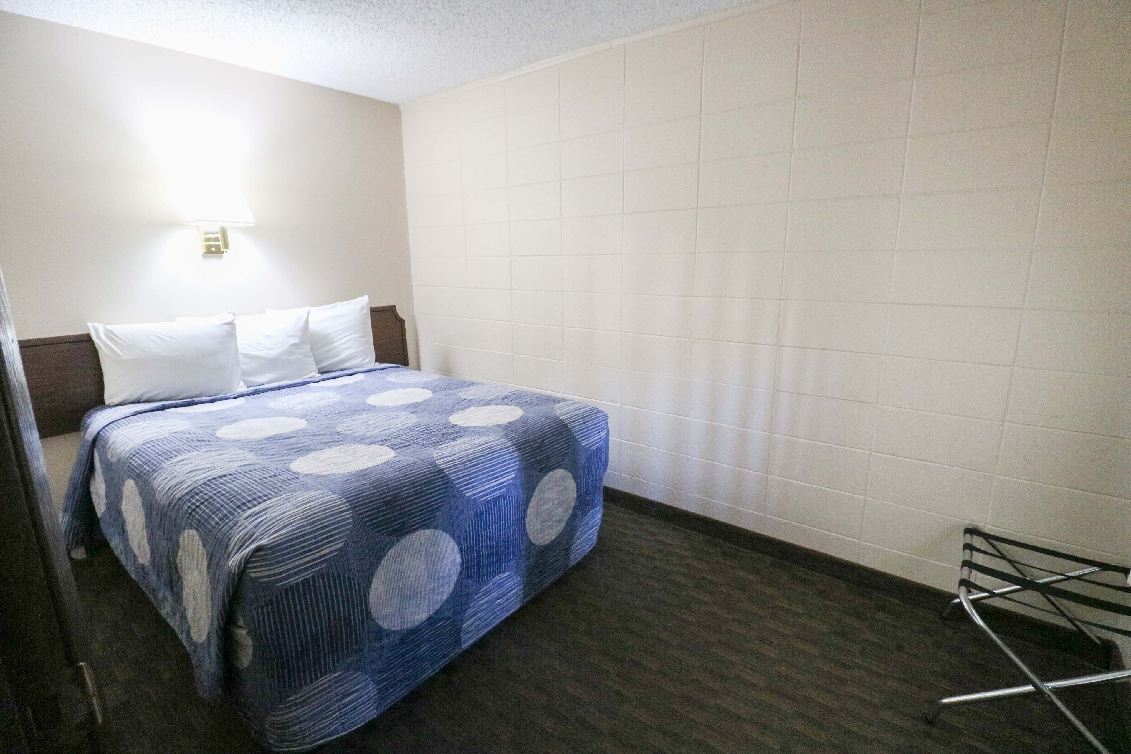 Habitación de hotel con una cama, una lámpara en la pared y un perchero metálico.