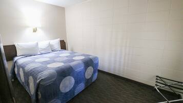 Habitación de hotel con una cama, una lámpara en la pared y un perchero metálico.