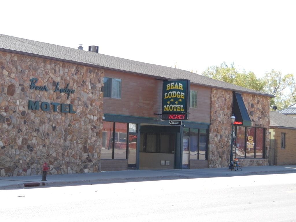 A Bear Lodge Motel with a stone facade, a 'VACANCY' sign, and a 'BEAR LODGE MUSEUM' sign.