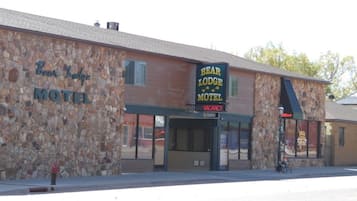 Motel Bear Lodge con fachada de piedra, un cartel de 'VACANCY' y un cartel que dice 'MUSEO BEAR LODGE'.
