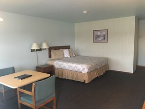 Una habitación de hotel con cama, mesita de noche, lámpara, silla y escritorio con una computadora portátil.