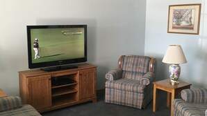 A living room with a television, a plaid armchair, a small table with a lamp, and a sofa. - Day's End Motel (Wisconsin Dells)