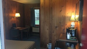 A room with wooden walls, a bed, a desk with a chair, a refrigerator, and a window with curtains. - Day's End Motel (Wisconsin Dells)